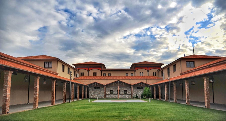 on side of 'Oenogenesis Estate' stone building with columns and green lawn in the front
